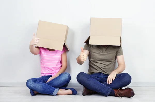 Couple with cardboard boxes on their heads sitting on floor near wall — Stock Photo, Image