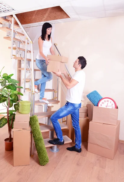 Jovem casal com caixas em nova casa no fundo escada — Fotografia de Stock