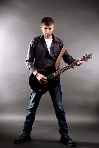 年轻的音乐家，弹吉他，在灰色的背景上 — 图库照片