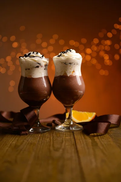 Sobremesa saborosa com chocolate, creme e molho de laranja, na mesa de madeira, no fundo das luzes — Fotografia de Stock