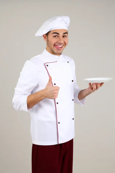 Professionele chef-kok in het witte uniform en hoed, op grijze achtergrond — Stockfoto