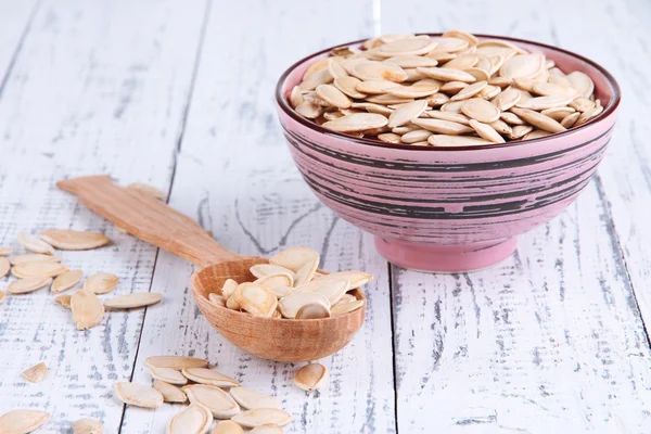 Pumpkin seeds in spoon and bowl on wooden background — Stock Photo, Image