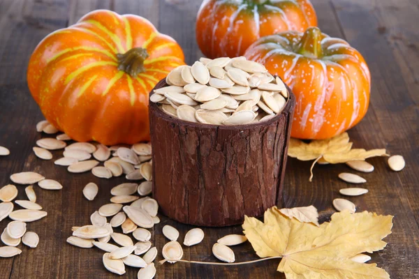 Pompoenpitten in pot met pumpkins op houten achtergrond — Stockfoto