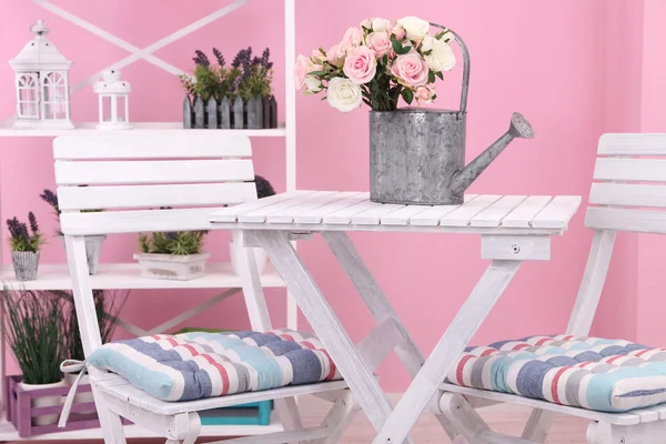 Стулья и стол с цветами на полках на розовом фоне — стоковое фото