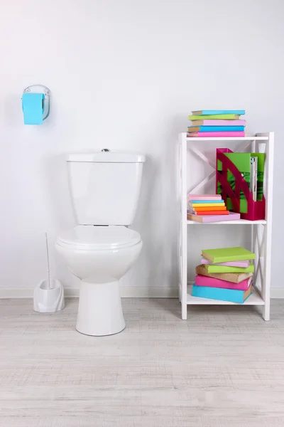 WC bianco ciotola e stand con libri, su sfondo parete a colori — Foto Stock