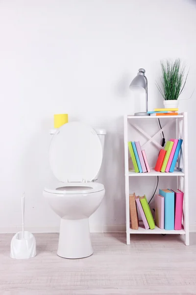 WC bianco ciotola e stand con libri, su sfondo parete a colori — Foto Stock