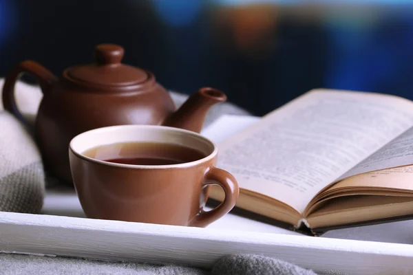 Xícara de chá quente com bule e livro na mesa em fundo brilhante — Fotografia de Stock