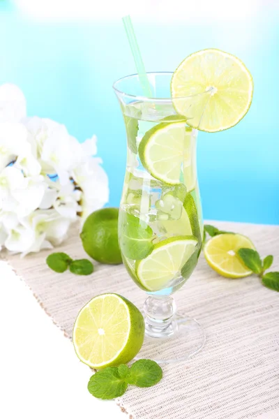 Glass of cocktail with lime and mint on table on light blue background — Stock Photo, Image