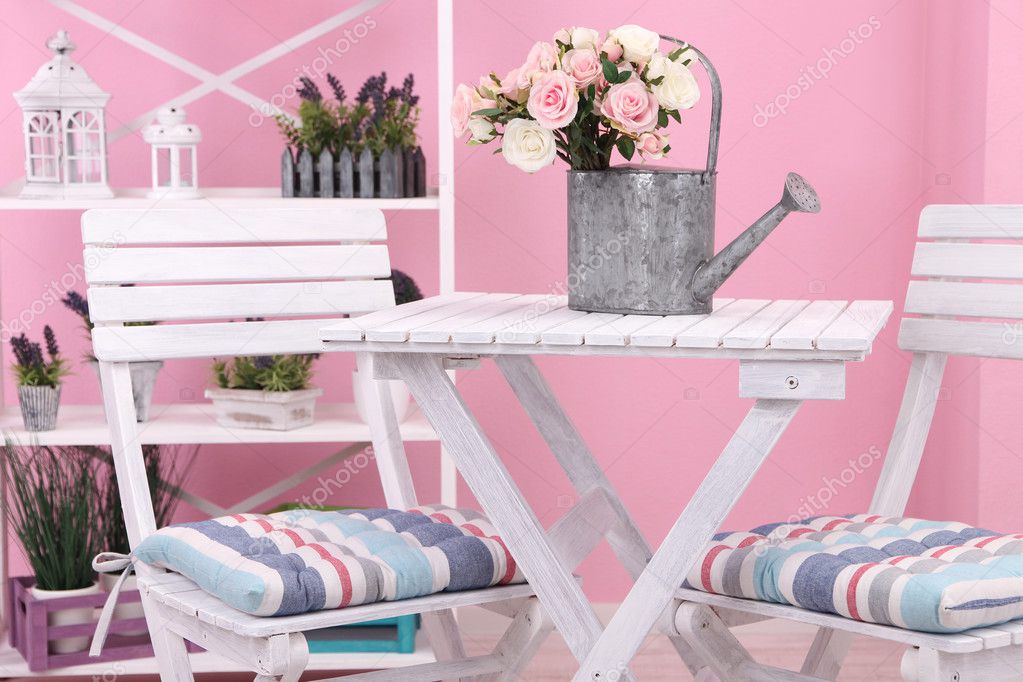 Garden chairs and table with flowers on shelves on pink background
