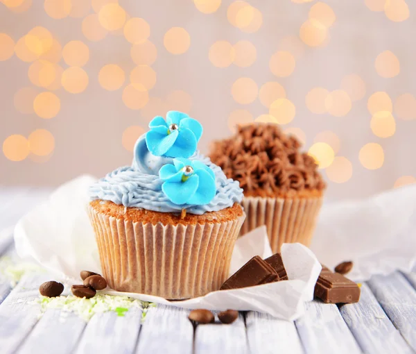 Smakelijke cupcakes met boter room, op kleur houten tafel, op lichten achtergrond — Stockfoto