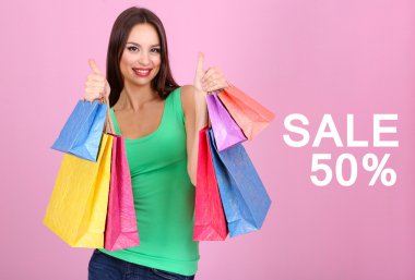 alışveriş torbaları pembe bir arka plan üzerinde tutan güzel genç kadın