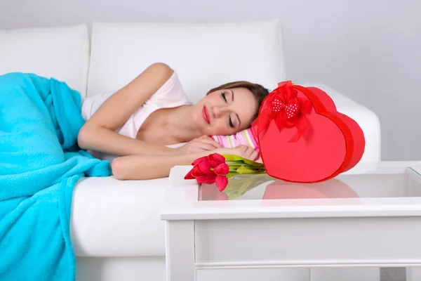 Hermosa joven que duerme en el sofá cerca de la mesa con regalos y flores, de cerca — Foto de Stock