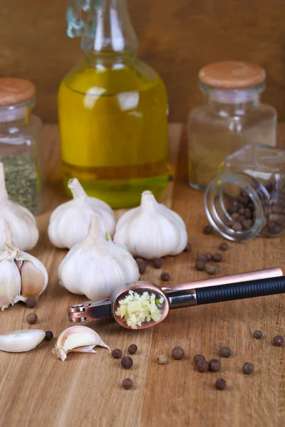 Samenstelling met knoflook press, verse knoflook en glazen potten met specerijen op houten achtergrond — Stockfoto