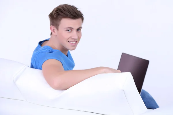 Парень сидит на диване с ноутбуком на белом фоне — стоковое фото