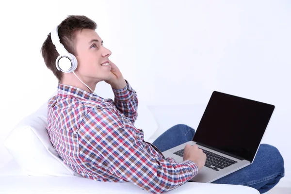 Cara sentado no sofá e ouvir música no fundo branco — Fotografia de Stock