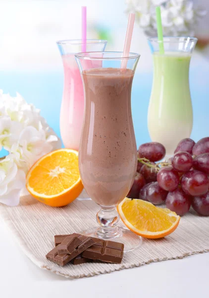 Milchshakes mit Früchten auf Tisch auf hellblauem Hintergrund — Stockfoto