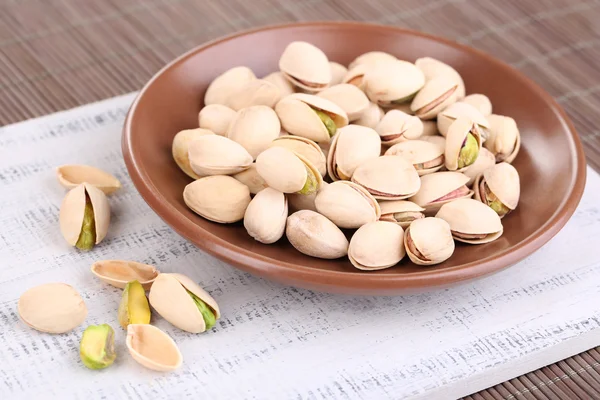 Pistachio nuts on plate on wooden background — Stock Photo, Image