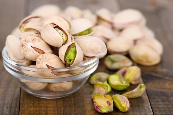 Pistachio nuts in glass bowl on wooden background — Stock Photo, Image