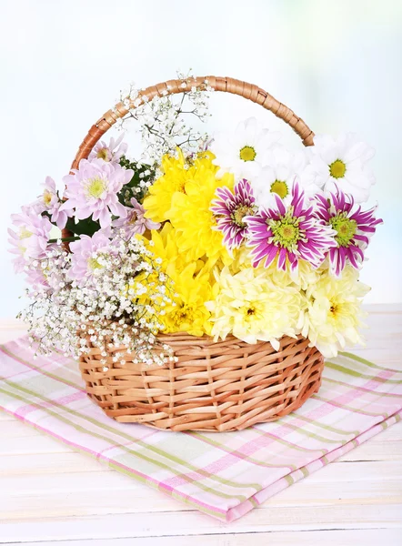 明るい背景にテーブルの上の枝編み細工品バスケットの美しい菊の花 — ストック写真