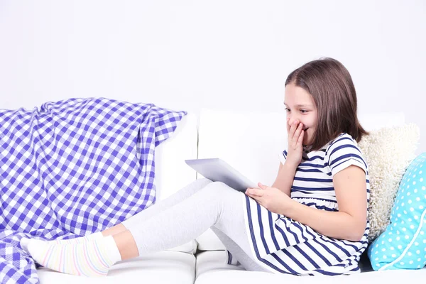 Menina bonita sentada no sofá com tablet, em casa fundo interior — Fotografia de Stock