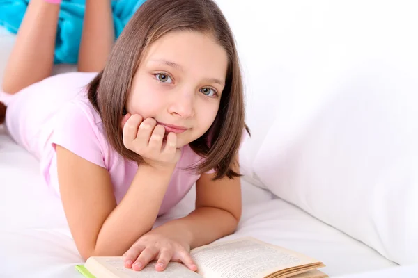 Beautiful little girl sitting on sofa with book, on home interior background Stock Photo