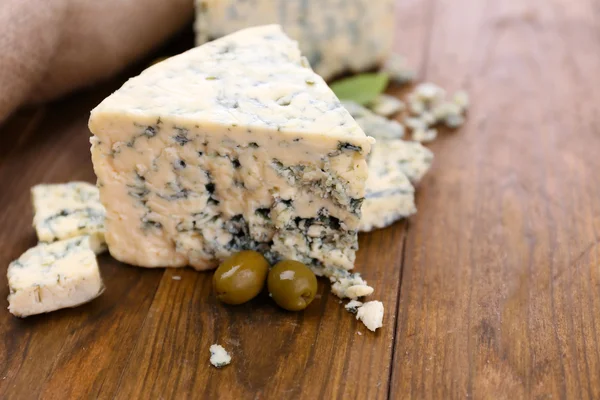 Smaczny ser pleśniowy z oliwkami i bazylią, na drewnianym stole — Zdjęcie stockowe