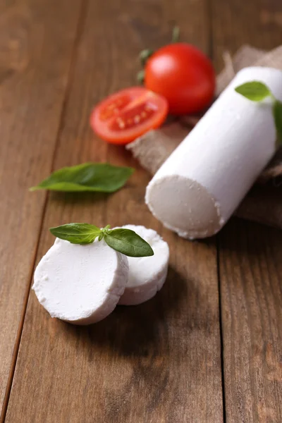 Tasty bushe cheese with basil and tomato, on wooden table — Stock Photo, Image