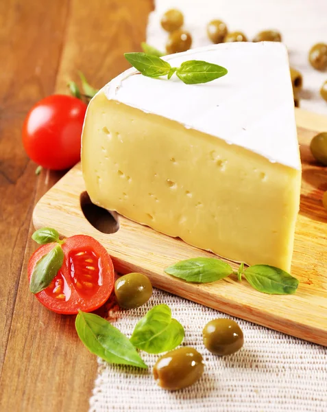 Tasty Camembert cheese with tomatoes, olives and basil, on wooden table — Stock Photo, Image