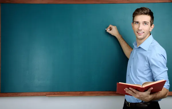 Young teacher near chalkboard in school classroom