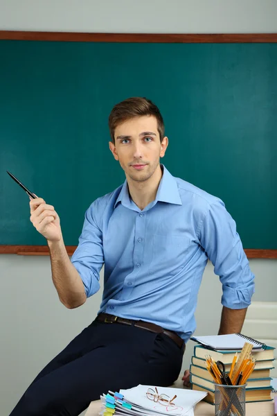 Fiatal tanár ül íróasztal iskolai tanteremben — Stock Fotó