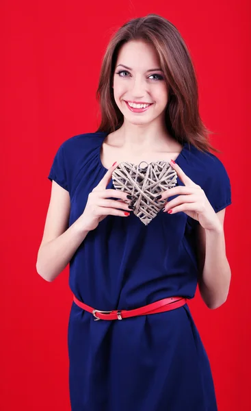 Attractive woman with wicker heart, on red background — Stock Photo, Image