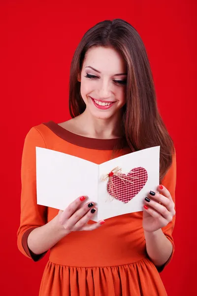 Aantrekkelijke vrouw met briefkaart, op rode achtergrond — Stockfoto