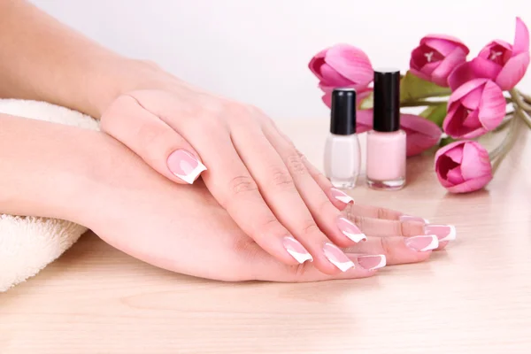 Belas mãos de mulher com manicure francês e flores na mesa no fundo branco — Fotografia de Stock