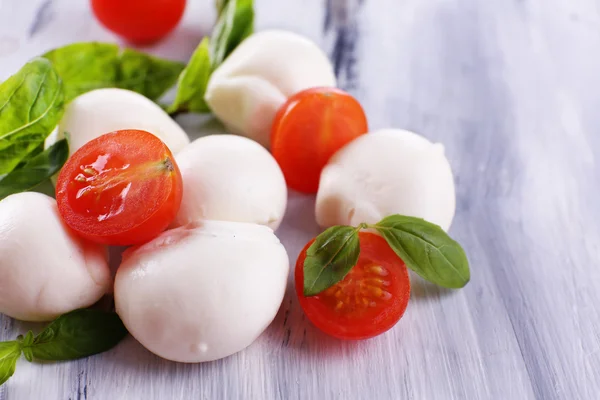 Tasty mozzarella cheese with basil and tomatoes, on wooden table — Stock Photo, Image