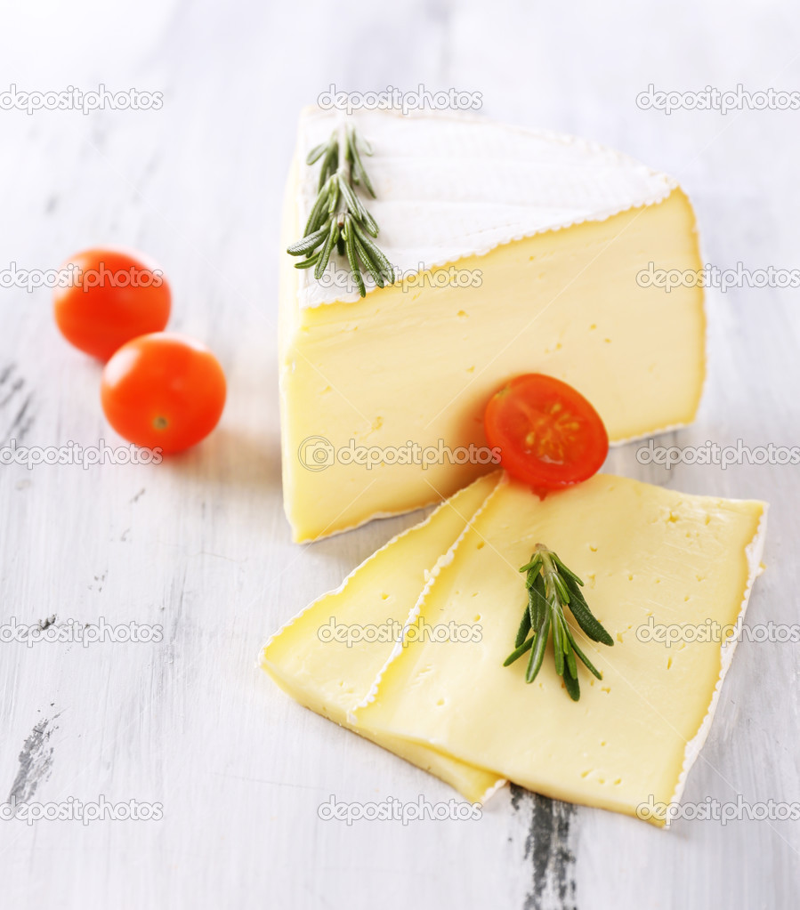 Tasty Camembert cheese with tomato and rosemary, on wooden table