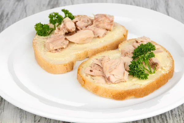 Roti lapis lezat dengan tuna dan ikan cod hati sarden, di piring putih. pada latar belakang kayu — Stok Foto
