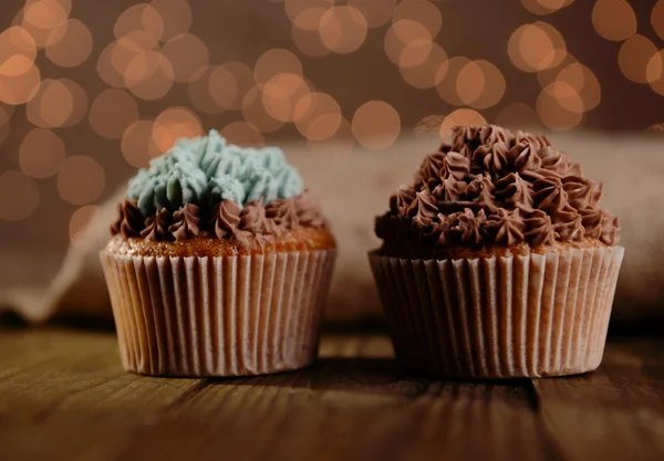 Sabrosos cupcakes con crema de mantequilla, sobre mesa de madera, sobre fondo de luces — Foto de Stock