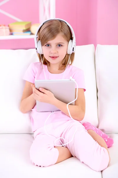 Little girl listening music sitting on sofa in room — Stock Photo, Image