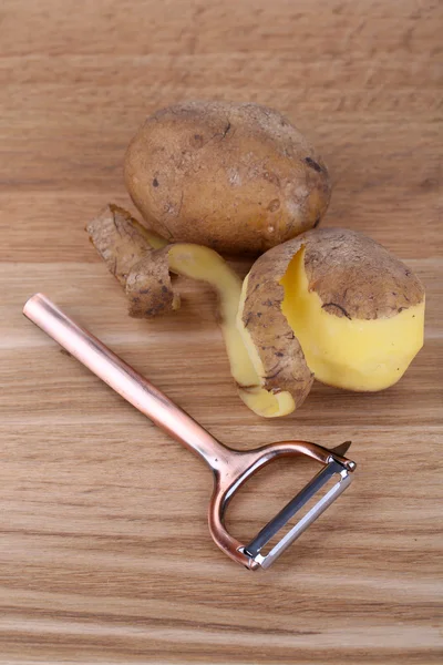 Pelapatate e patate fresche su fondo di legno — Foto Stock