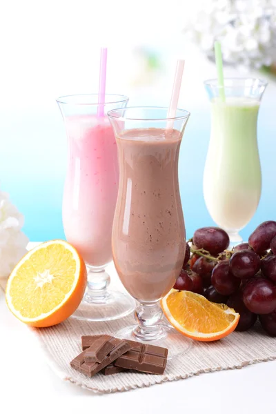 Melk schudt met vruchten op tafel op lichte blauwe achtergrond — Stockfoto
