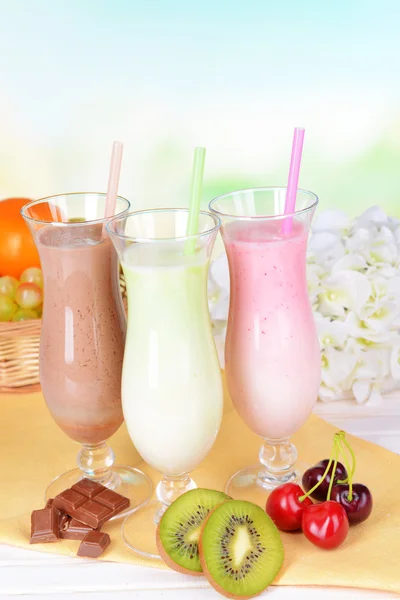 Melk schudt met vruchten op tafel op lichte blauwe achtergrond — Stockfoto