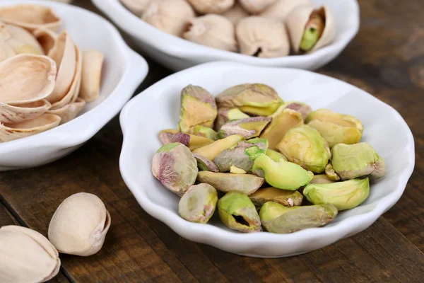 Pistachio nuts in small bowls on wooden background — Stock Photo, Image