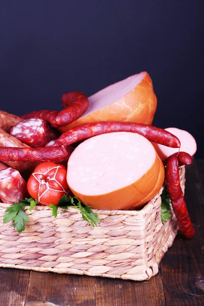 Beaucoup de différentes saucisses dans le panier sur une table en bois sur fond noir — Photo