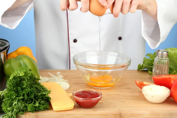 Female hands break egg into glass bowl, on blue background — Stock Photo, Image