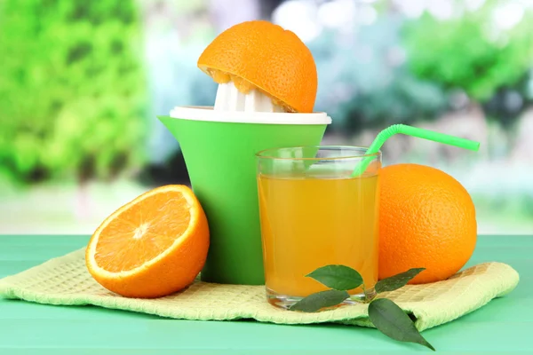 Narenciye sıkacağı, cam suyu ve yeşil ahşap masa üzerinde olgunlaşmış portakal — Stok fotoğraf