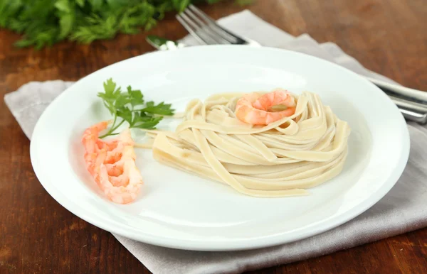 Pasta med räkor på vit platta, på trä bakgrund — Stockfoto