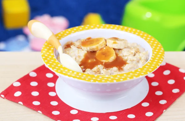 Tigela de mingau de cereal para bebê e brinquedos na mesa, no fundo de brinquedos — Fotografia de Stock