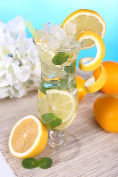 Glass of cocktail with lemon and mint on table on light blue background — Stock Photo, Image