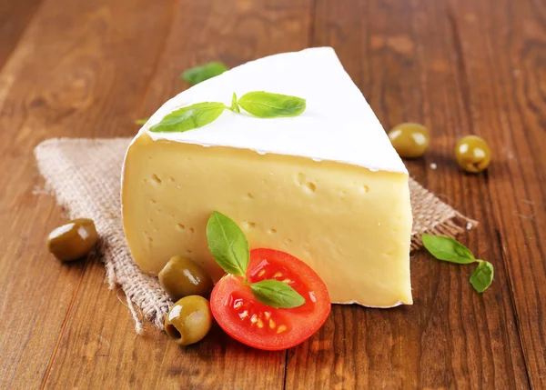 Tasty Camembert cheese with tomato, basil and olives, on wooden table — Stock Photo, Image