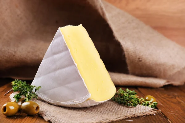 Tasty Camembert cheese with thyme and olives, on wooden table — Stock Photo, Image